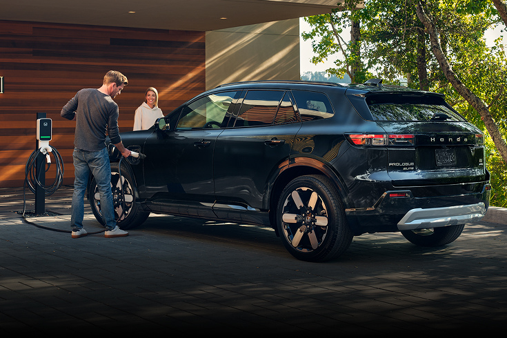 2024 Honda Prologue Elite in Raven Black profile being charged at a home charging station (All-Electric SUV).