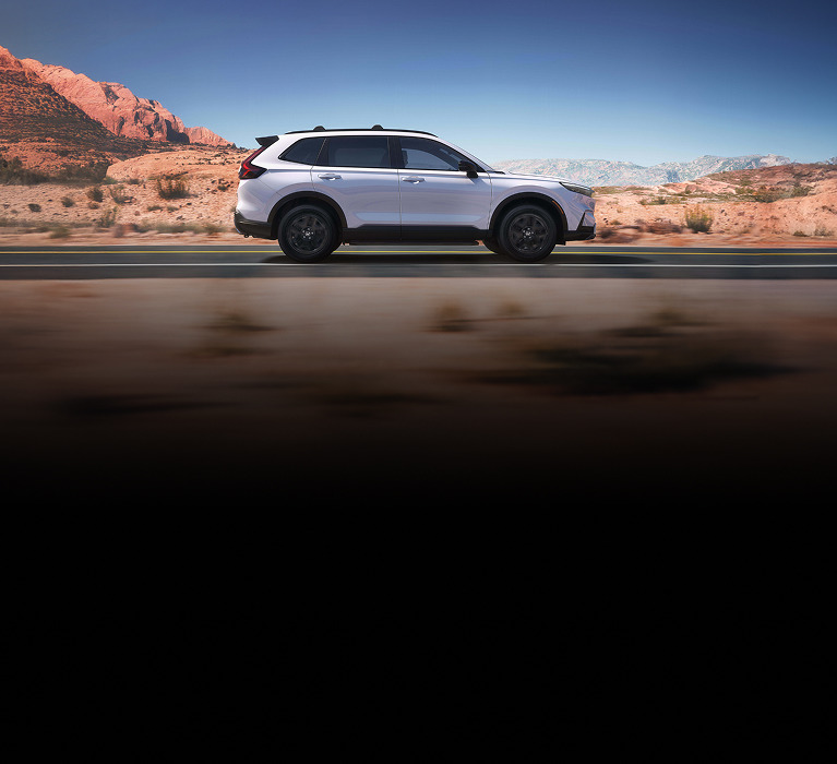 2026 Honda CR-V Sport Touring Hybrid in Platinum White Pearl profile driving along a scenic road (Compact Crossover SUV).